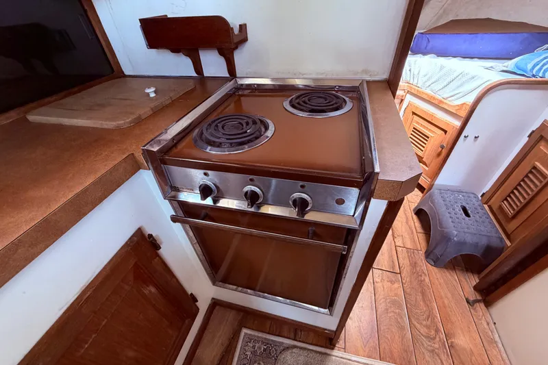 Slide: The Image of 1978 Mainship 34 Trawler kitchen with stove, wooden cabinetry, and cozy interior. - 48