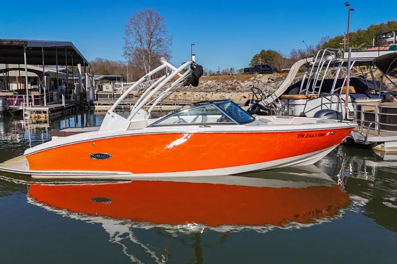 The Image of 2023 Cobalt CS22 boat with vibrant orange hull docked at a marina. - 0