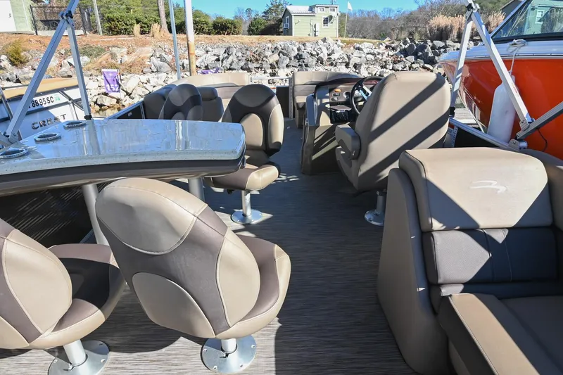 Slide: The Image of 2021 Bennington SX 23 Entertainment boat interior with seating and table, docked by rocky shore. - 6