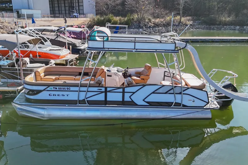 The Image of 2023 Crest Caribbean LX 250 pontoon boat with slide, docked on calm green water. - 0