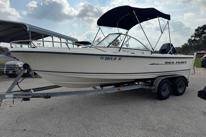 The Image of 2000 Sea Hunt Escape 200 boat on trailer with canopy, parked outdoors. - 1