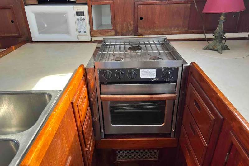 Slide: The Image of 1980 Wellington 44 Cutter Center Cockpit kitchen with stove, microwave, and wooden cabinetry. - 25