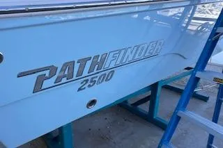 Slide: The Image of 2024 Pathfinder 2500 Hybrid boat hull on a blue stand in a workshop. - 2