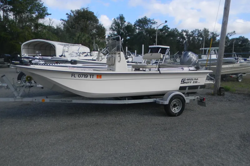 Slide: The Image of 2024 Carolina Skiff e-18 boat on trailer, parked outdoors with other boats. - 10
