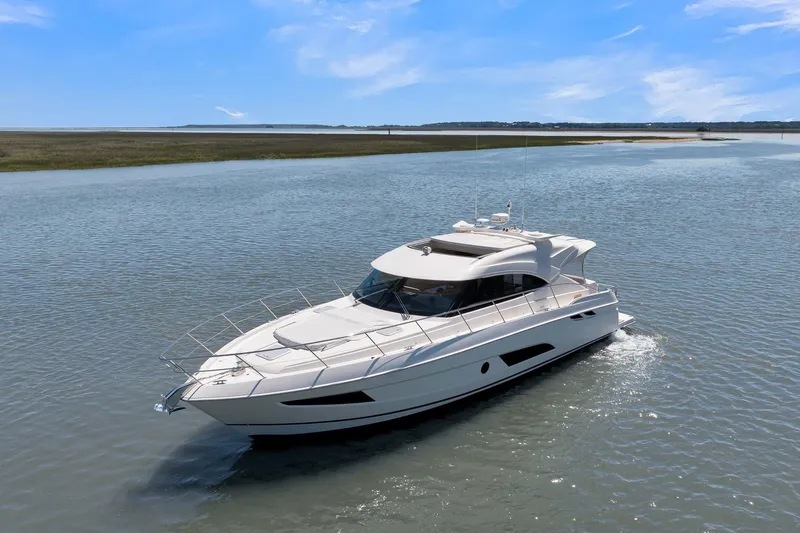 Slide: The Image of 2020 Riviera 4800 Sport Yacht cruising on a serene waterway under a clear blue sky. - 11