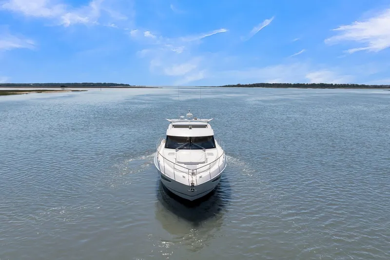 Slide: The Image of 2020 Riviera 4800 Sport Yacht cruising on a serene, open waterway under a clear blue sky. - 13