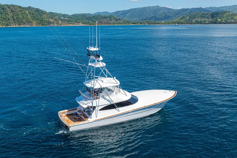 Slide: The Image of 2026 Viking 64 Convertible yacht cruising on blue ocean near lush green coastline. - 55