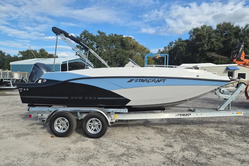 The Image of 2026 Starcraft SVX 191 OB boat on trailer, parked outdoors under a blue sky. - 1