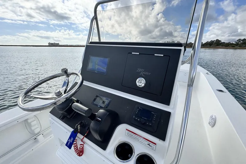 Slide: The Image of 2024 Bay Rider 2460 Skiff console with steering wheel and navigation equipment on calm water. - 17