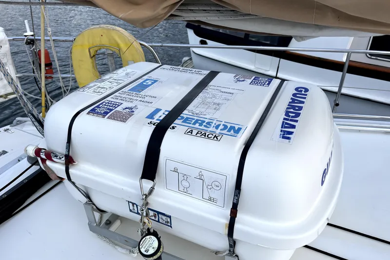 Slide: The Image of Liferaft on 1979 Amel Mango sailboat, secured with straps, docked by the water. - 23