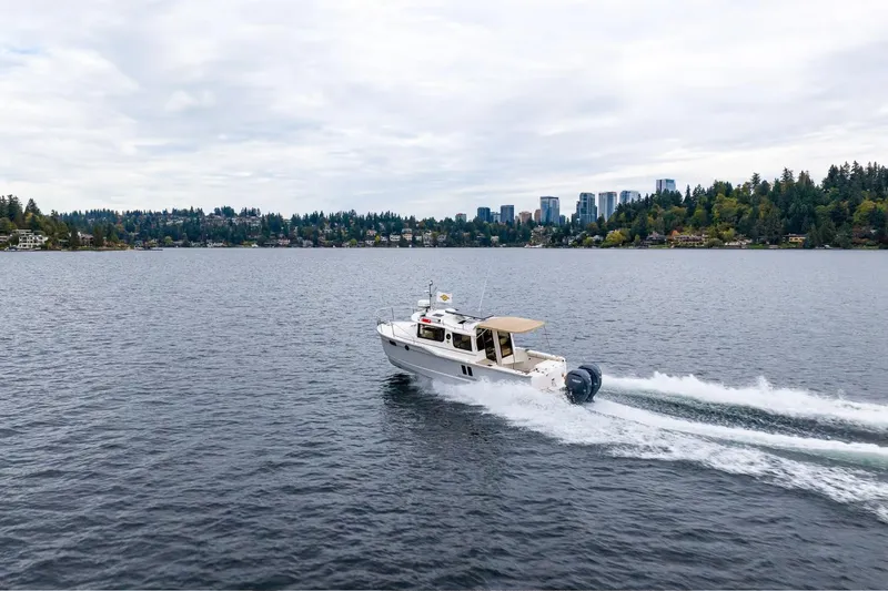 Slide: The Image of 2026 Ranger Tugs R-27 cruising on a scenic lake with city skyline backdrop. - 15