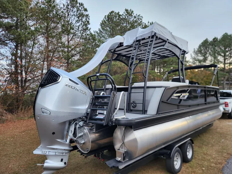 Slide: The Image of 2025 Godfrey AquaPatio Sundeck 275 SDC pontoon boat on trailer, parked outdoors. - 2