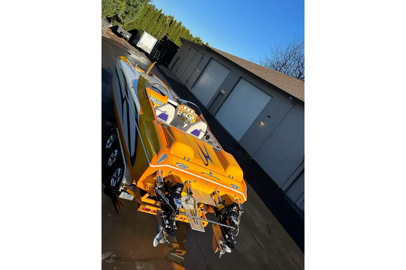 Slide: The Image of 2007 Eliminator Daytona 30 boat with vibrant orange design, parked near garages. - 42