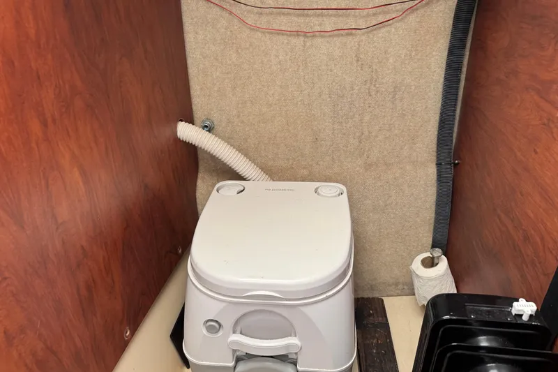 Slide: The Image of Portable toilet inside 2005 MacGregor 26M Powersailer, with wooden paneling and plumbing hoses. - 28