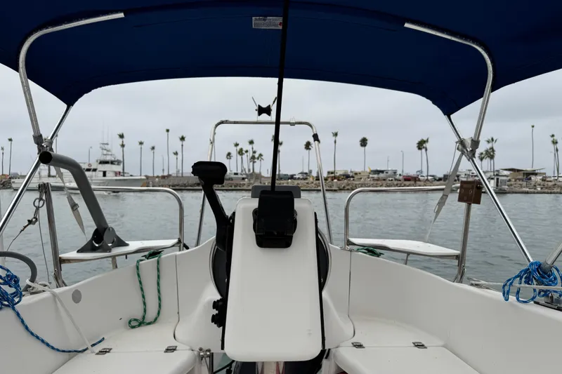 Slide: The Image of 2005 MacGregor 26M Powersailer cockpit with blue canopy, docked near palm-lined shore. - 8