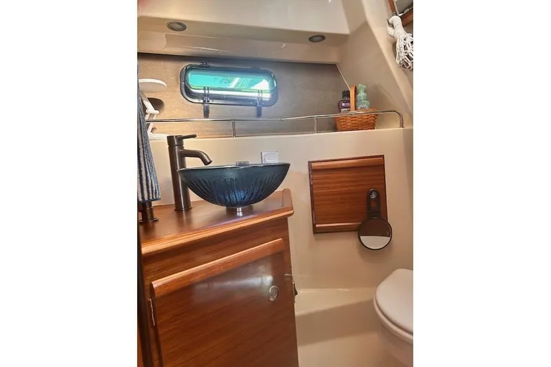 Slide: The Image of 2024 Ranger Tugs R-27 bathroom with modern sink, wooden cabinetry, and porthole window. - 17