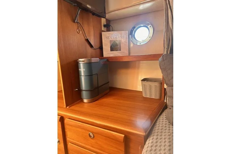 Slide: The Image of 2024 Ranger Tugs R-27 interior with wooden cabinetry, porthole, and Keurig coffee maker. - 21