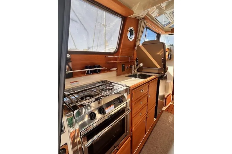 Slide: The Image of 2024 Ranger Tugs R-27 interior kitchen with stove, sink, and wooden cabinetry. - 5