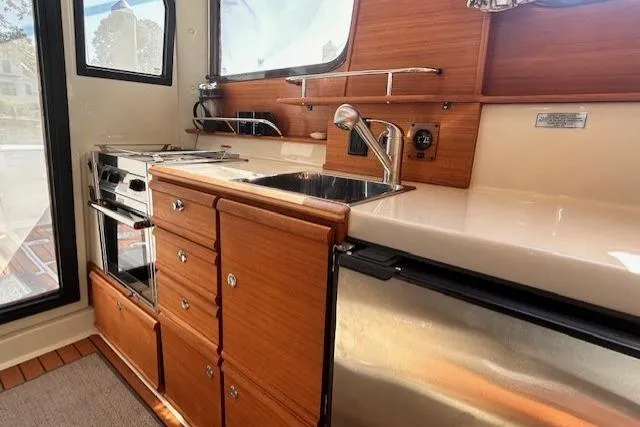 Slide: The Image of 2024 Ranger Tugs R-27 interior kitchen with wood cabinetry, sink, and stainless steel appliances. - 7