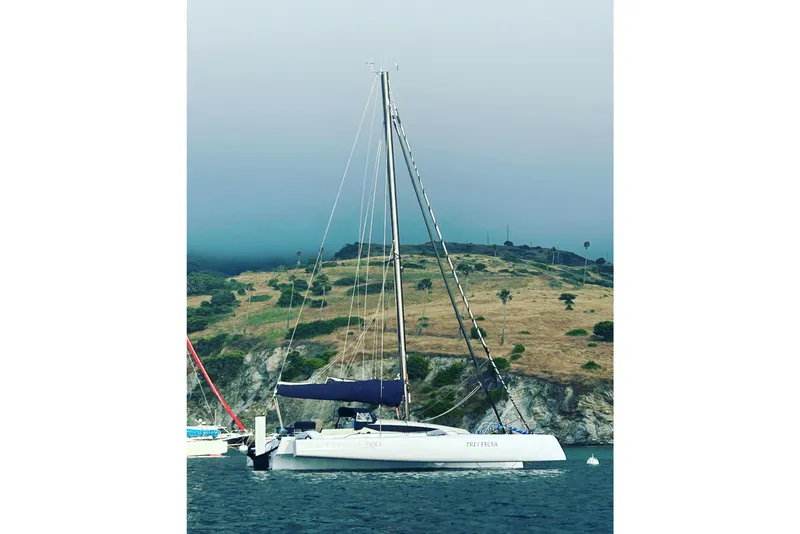 The Image of 2022 Corsair 880 Standard sailboat anchored near a scenic, hilly coastline. - 0