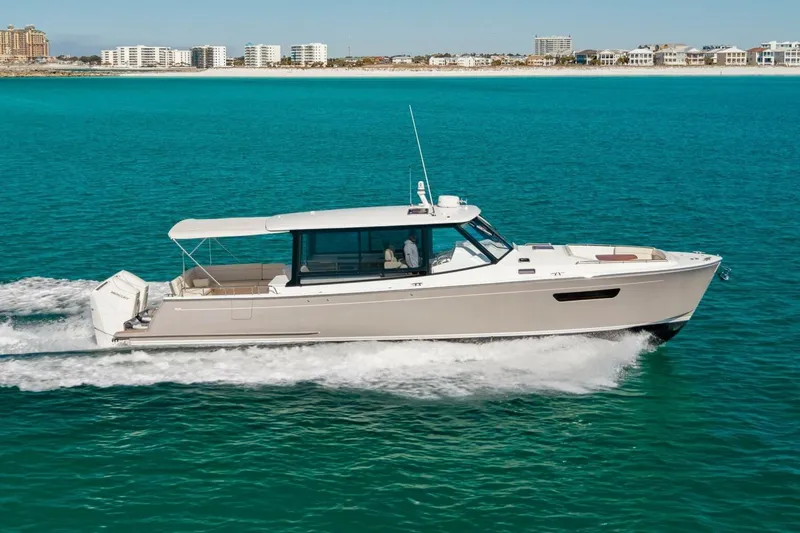 The Image of 2025 MJM 4 boat cruising on turquoise water near a coastal cityscape. - 6