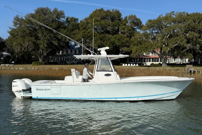 The Image of 2020 Regulator 31 boat on calm water, surrounded by trees and a house in the background. - 0