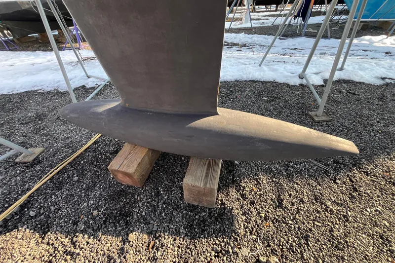 Slide: The Image of Keel of 2007 Beneteau First 10R sailboat on wooden blocks, gravel and snow background. - 13