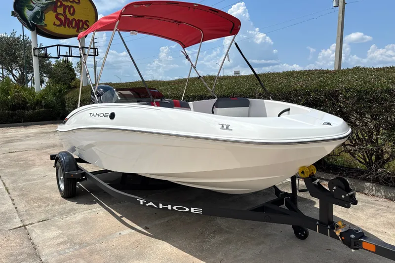 Slide: The Image of 2026 Tahoe T16 boat with red canopy on trailer, parked outdoors. - 5