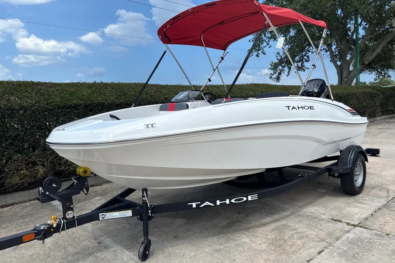 Slide: The Image of 2026 Tahoe T16 boat with red canopy on trailer, parked outdoors under blue sky. - 1