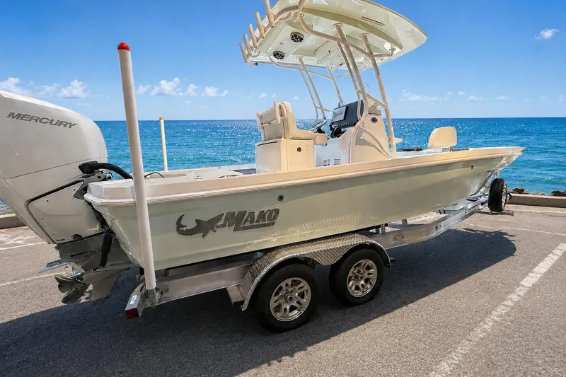 The Image of 2026 Mako 24 APEX boat on trailer by the ocean, featuring Mercury engine. - 0