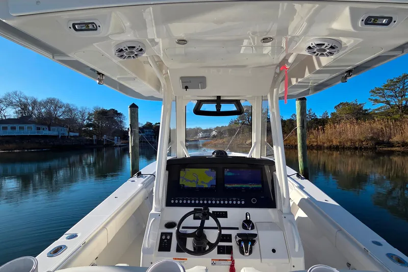 Slide: The Image of 2021 Regulator 34 boat cockpit with navigation screens, steering wheel, and serene waterway view. - 21
