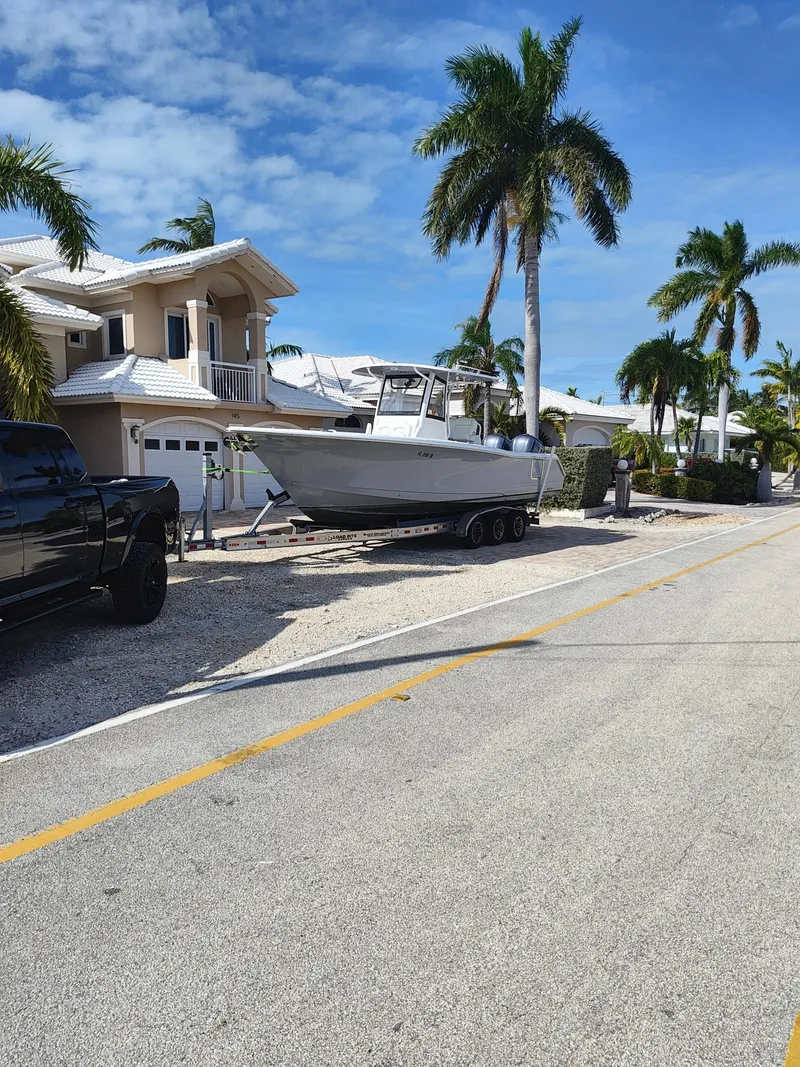 Slide: The Image of 2018 Sea Hunt Gamefish 30 boat on trailer, parked near palm trees and houses. - 8
