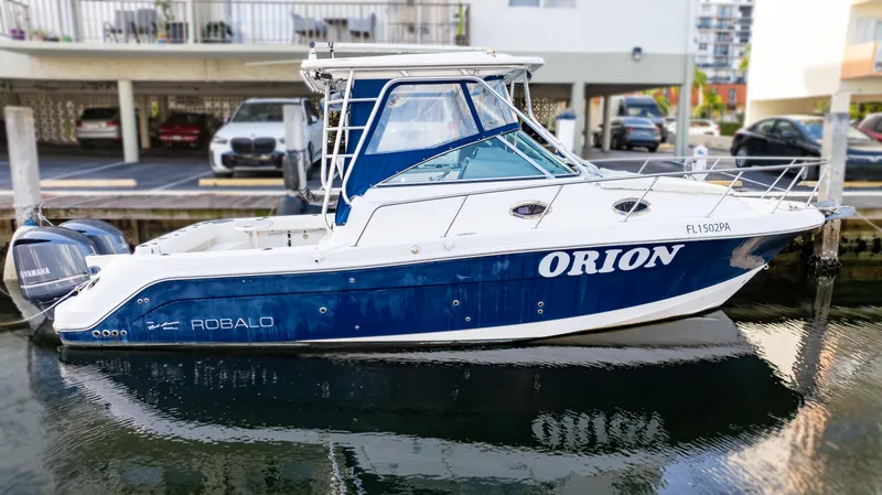 Slide: The Image of 2010 Robalo R305 Walkaround boat docked, featuring blue and white design. - 90