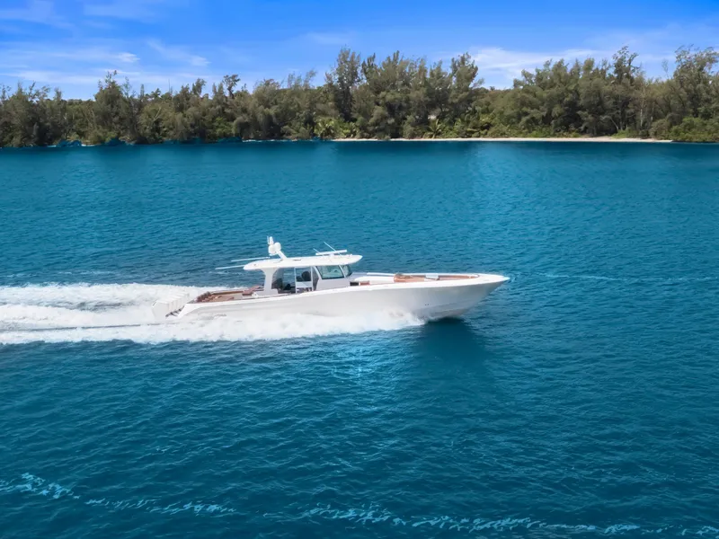 Slide: The Image of 2023 HCB 65 Estrella cruising on blue water near a forested shoreline. - 1