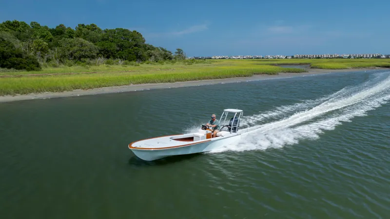 Slide: The Image of 2023 Custom Carolina 18 Flats boat cruising on a scenic waterway. - 2
