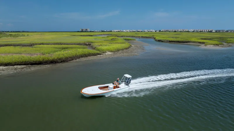 Slide: The Image of 2023 Custom Carolina 18 Flats boat cruising through scenic marshland waters. - 3
