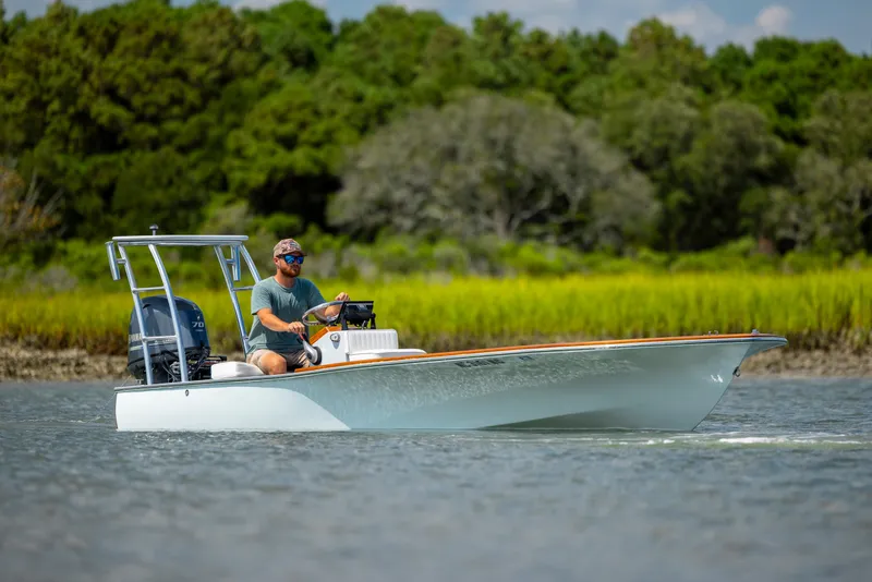 Slide: The Image of 2023 Custom Carolina 18 Flats boat cruising on a calm river with lush green background. - 7
