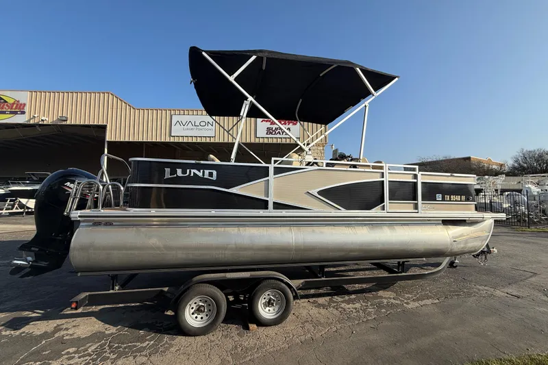 Slide: The Image of 2020 Lund LX220 Pontoon Fish boat on trailer, with canopy, parked outdoors. - 2