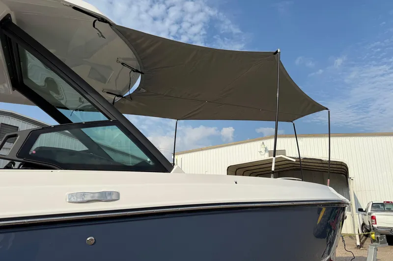 Slide: The Image of 2026 Monterey Elite 25 OB boat with canopy, parked near a warehouse under a blue sky. - 22
