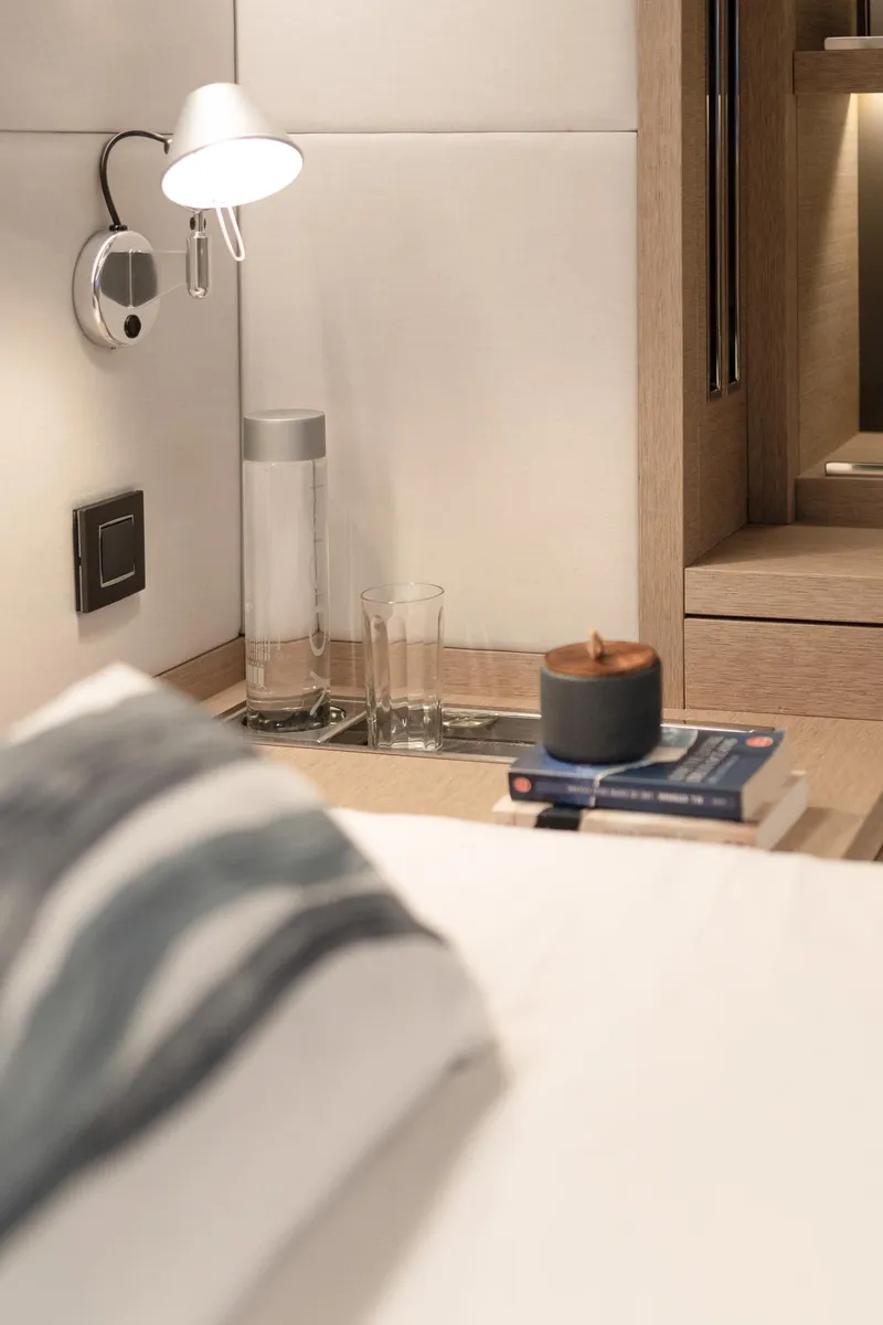 Slide: The Image of Luxurious Lagoon SIXTY 5 yacht interior, featuring a cozy bedside setup with books and a lamp. - 28