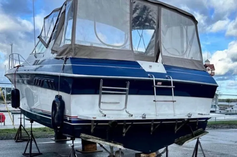 Slide: The Image of 1987 Wellcraft 3400 Gran Sport boat on stands, blue and white exterior, marina background. - 16