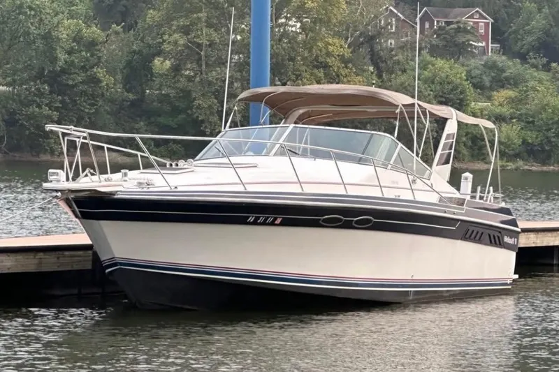 Slide: The Image of 1987 Wellcraft 3400 Gran Sport boat docked on a calm lake with lush greenery. - 4