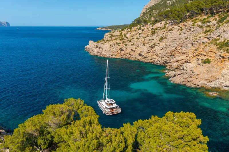 Slide: The Image of 2025 Lagoon 60 yacht anchored in a serene, rocky coastal bay with clear blue waters. - 5