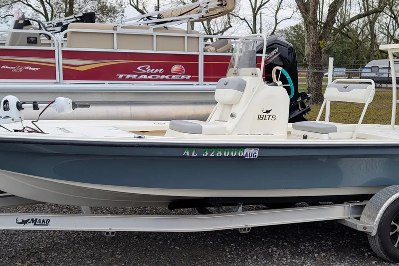 The Image of 2023 Mako 18 LTS boat on trailer, parked beside a Sun Tracker pontoon. - 1