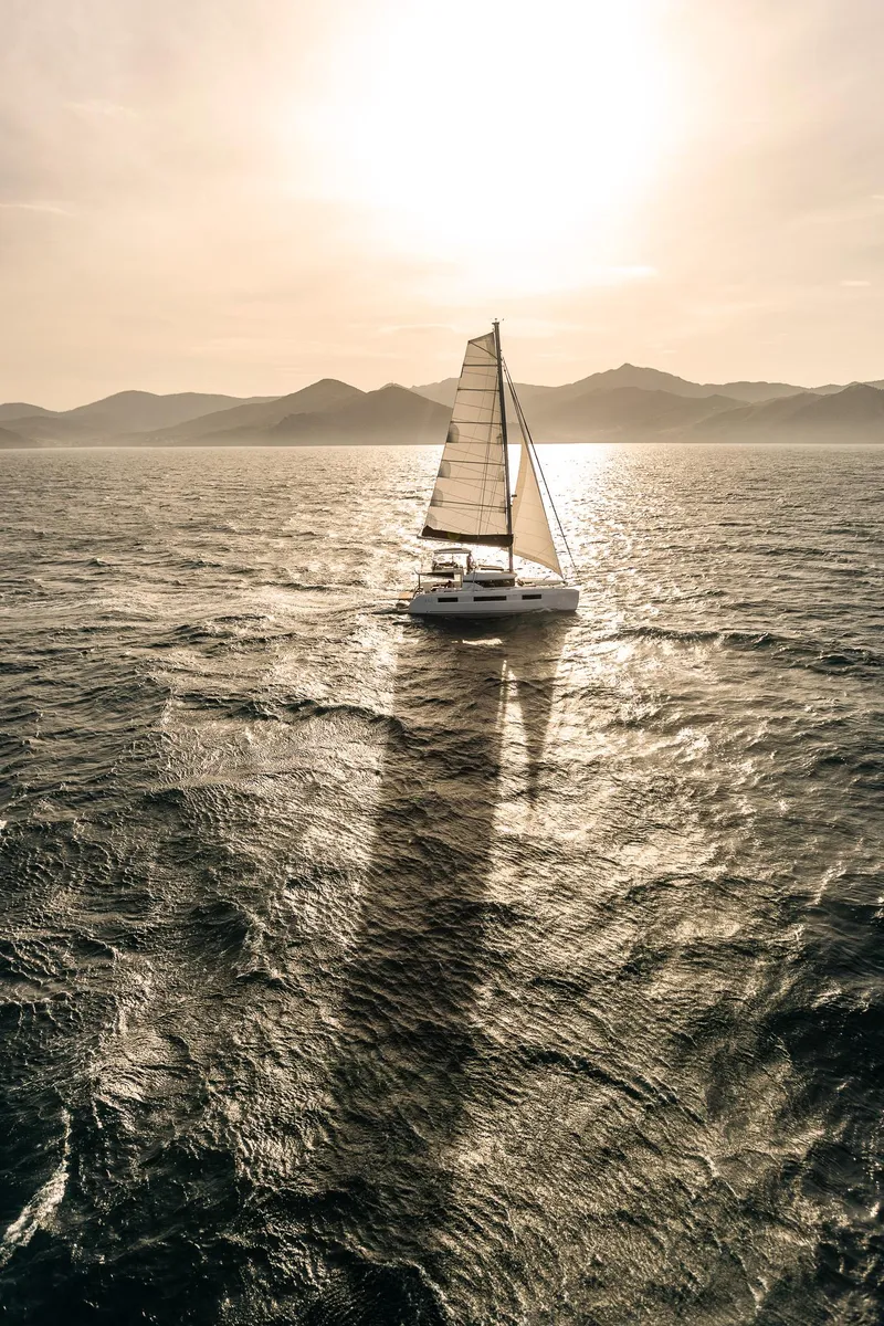 Slide: The Image of Sailing Lagoon 51 ICONIC 2025 catamaran on sunlit ocean with mountainous horizon. - 24