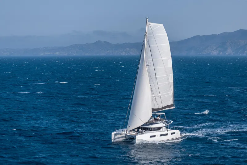 Slide: The Image of 2025 Lagoon 51 ICONIC catamaran sailing on open sea with mountainous backdrop. - 26