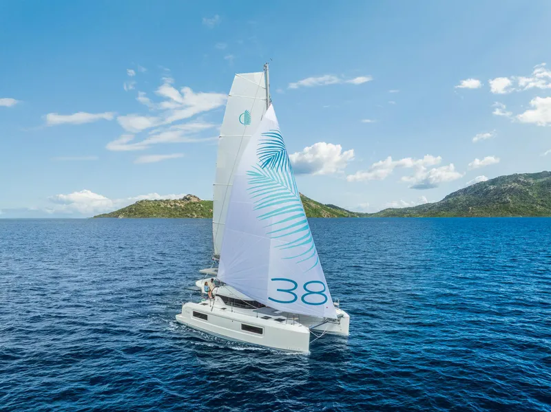 Slide: The Image of 2025 Lagoon 38 catamaran sailing on blue ocean with scenic island backdrop. - 4
