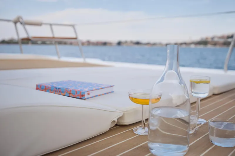 Slide: The Image of Luxurious deck of 2025 Omaya 50 Power Catamaran with drinks and book, overlooking serene water. - 24