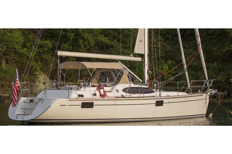 Slide: The Image of Manufacturer Provided Image: 2025 Hylas H48 sailboat with American flag, anchored near lush greenery. - 2