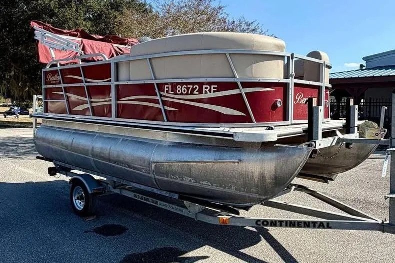 Slide: The Image of 2017 Bentley Pontoons 140 Cruise on trailer, red and silver design, parked outdoors. - 3